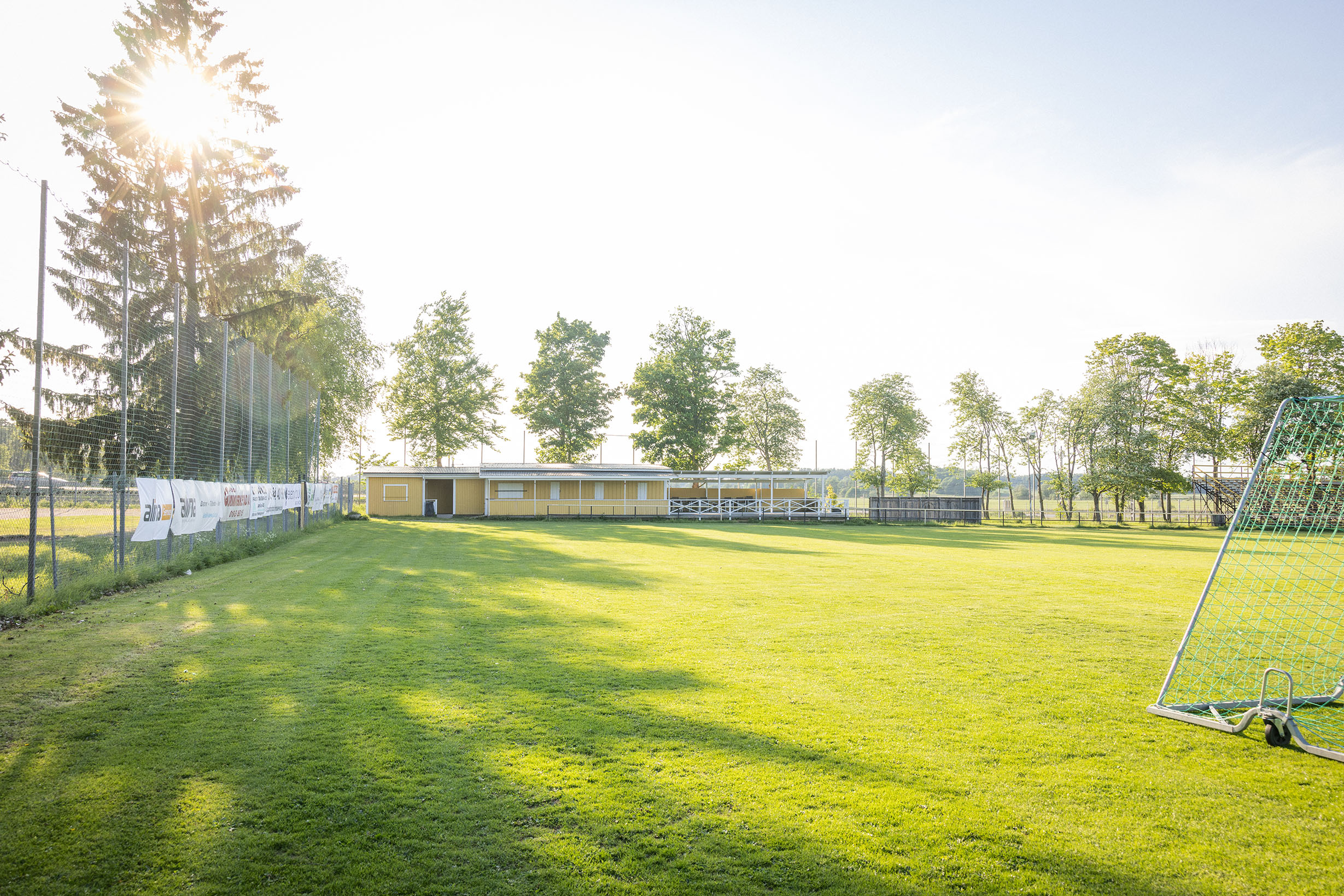 Fotbollsplan med grönt gräs framför gula träbyggnader