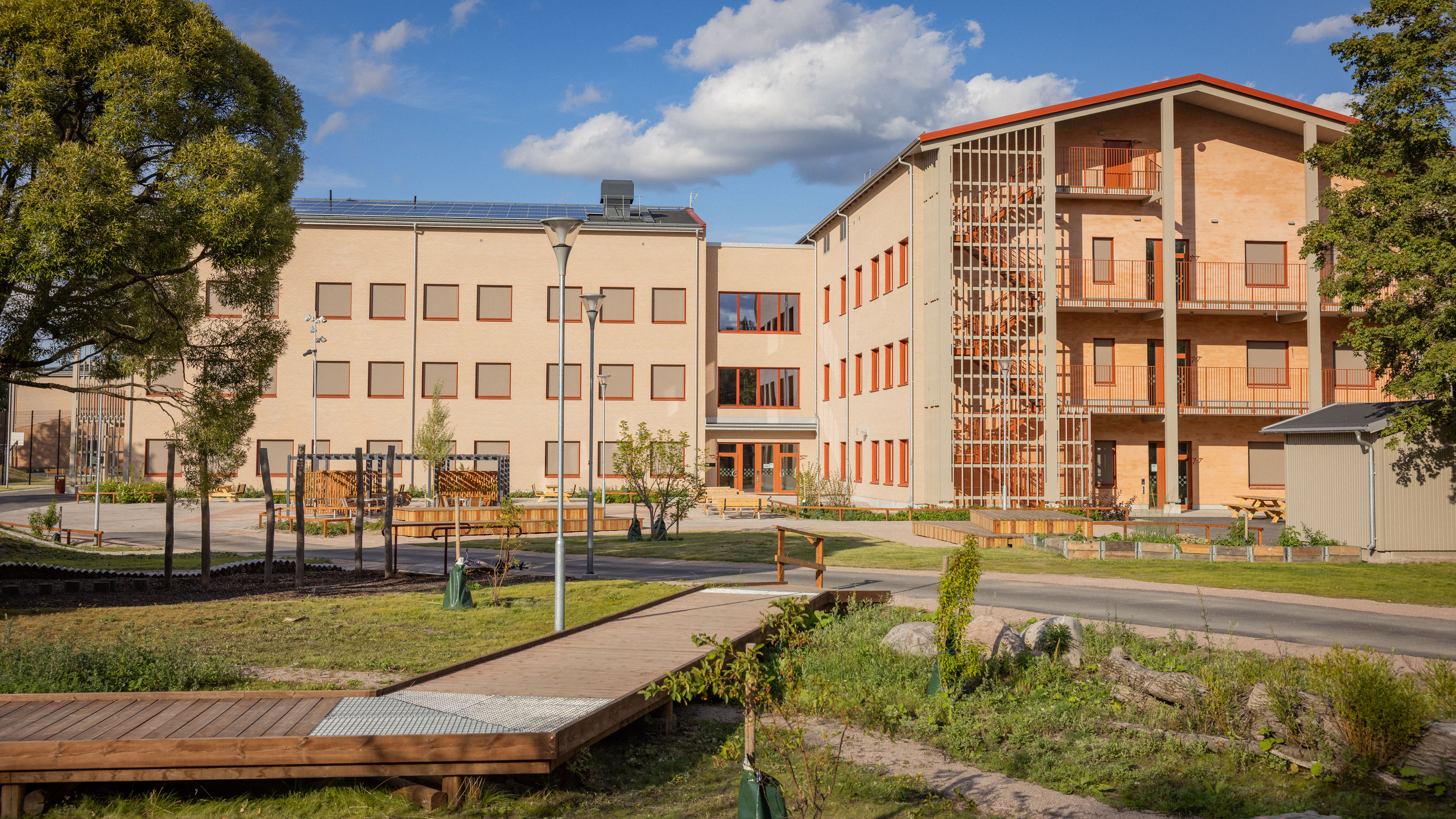 Nybyggd skola med ljusbrunt tegel, röda fönster och lekutrustning i förgrunden.