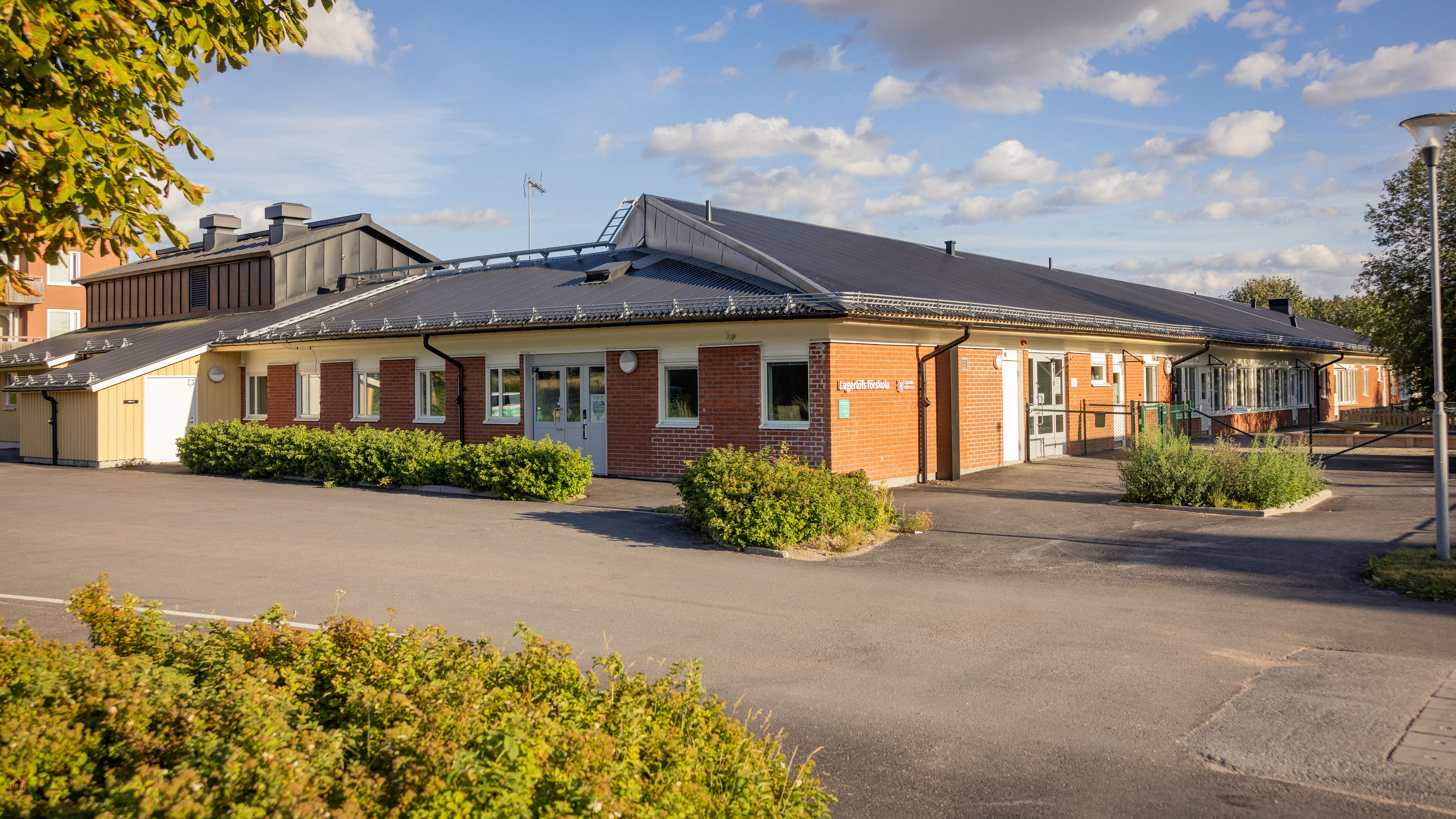 Nyrenoverad förskola med brunt tegel och gröna buskar i förgrunden.